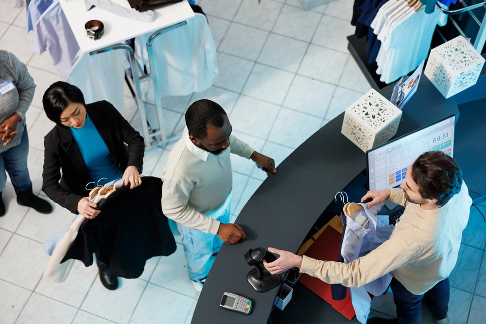 Cashier at clothing store checkout desk scanning and processing purchase for customer top view