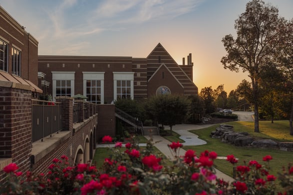 Exterior of World Outreach Church in Tennessee at sunset, featuring red flowers, brick architecture, landscaped grounds, and walking paths.
