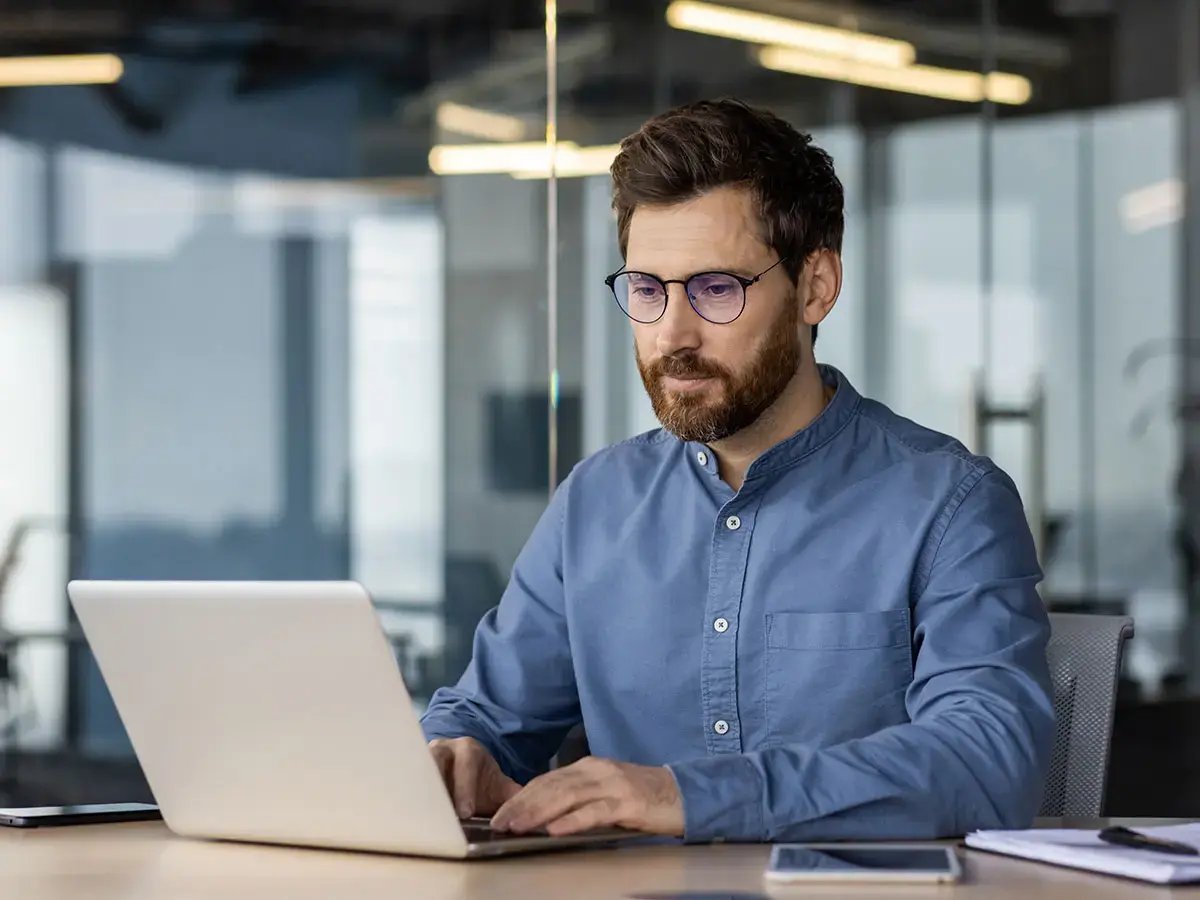 A man with glasses types on a laptop in a modern office.