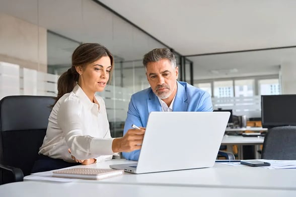 A woman and man discuss over a laptop in an office