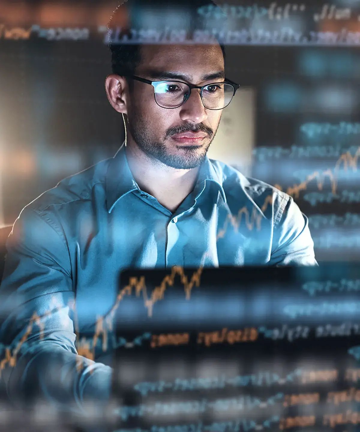 A man in glasses and a blue shirt focuses on a computer screen. Transparent graphs and data overlay suggest analysis, conveying a tech-driven atmosphere.