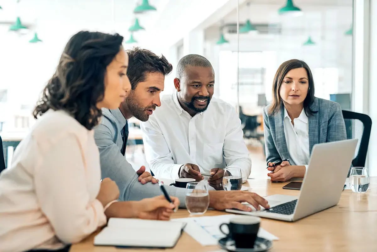 Professionals are collaborating around a laptop in a modern office setting.
