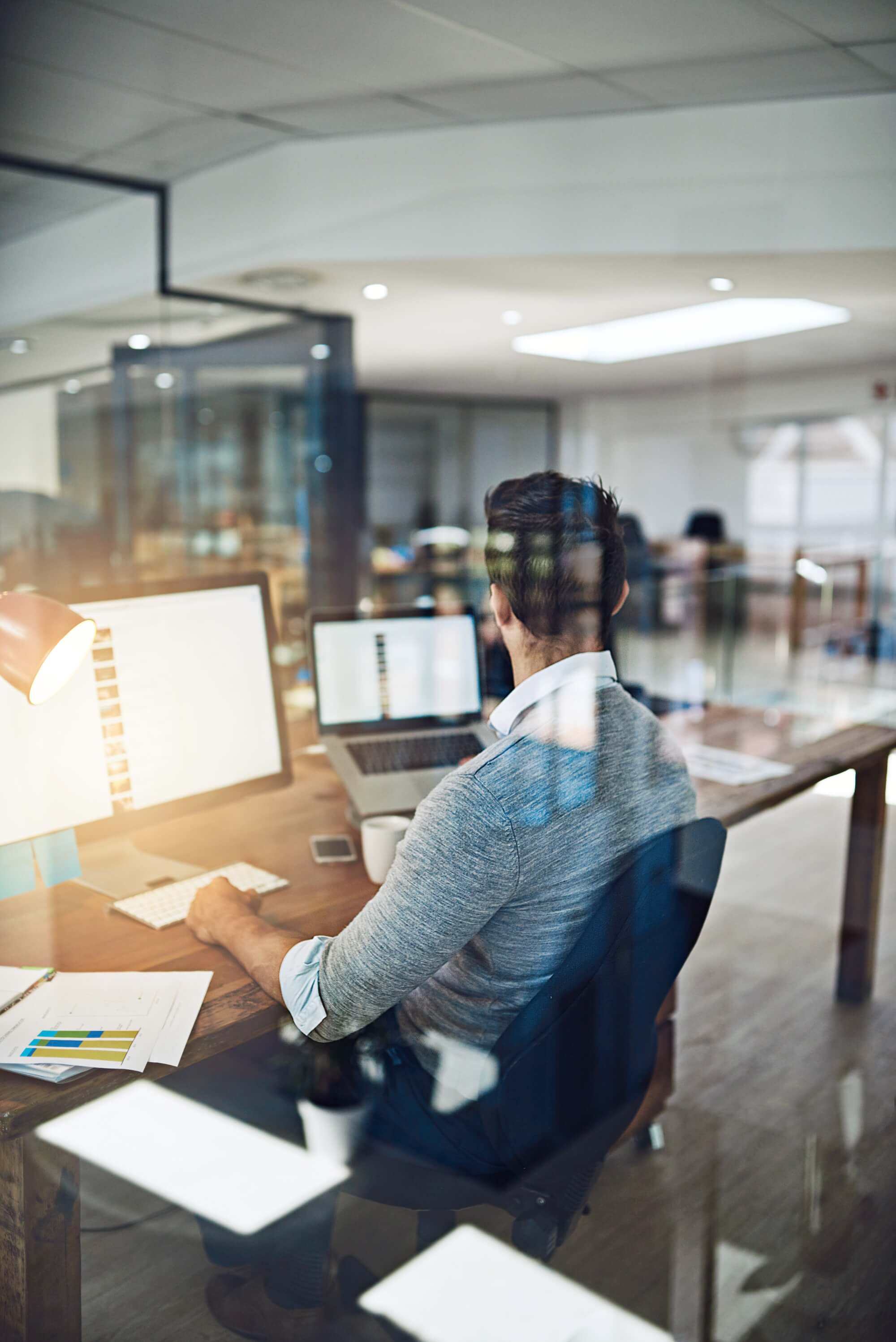 Man sitting at desk in office setting looking at computer screens