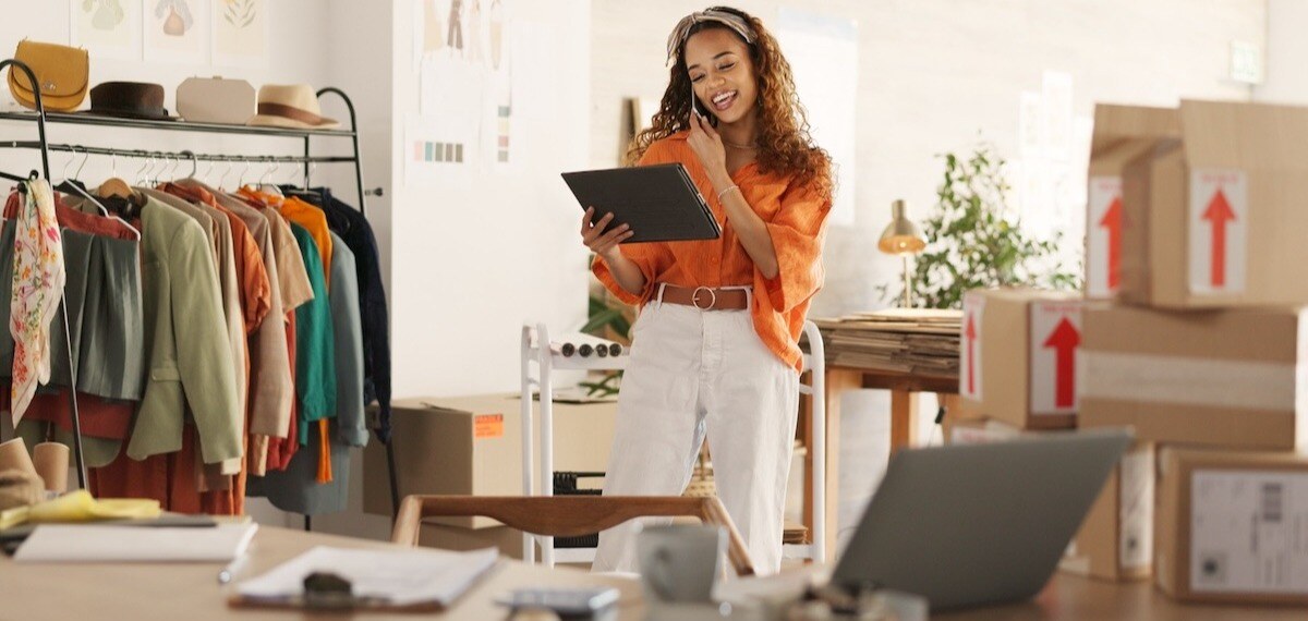 A woman utilizing a tablet integrates retail IT solutions to enhance cyber resiliency in her retail business, surrounded by inventory.