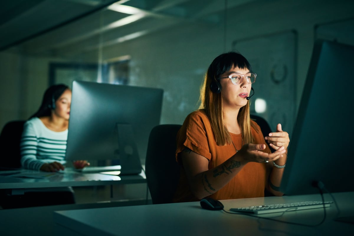 Woman sitting on her desk in a dark room having a virtual meeting while explaining a topic
