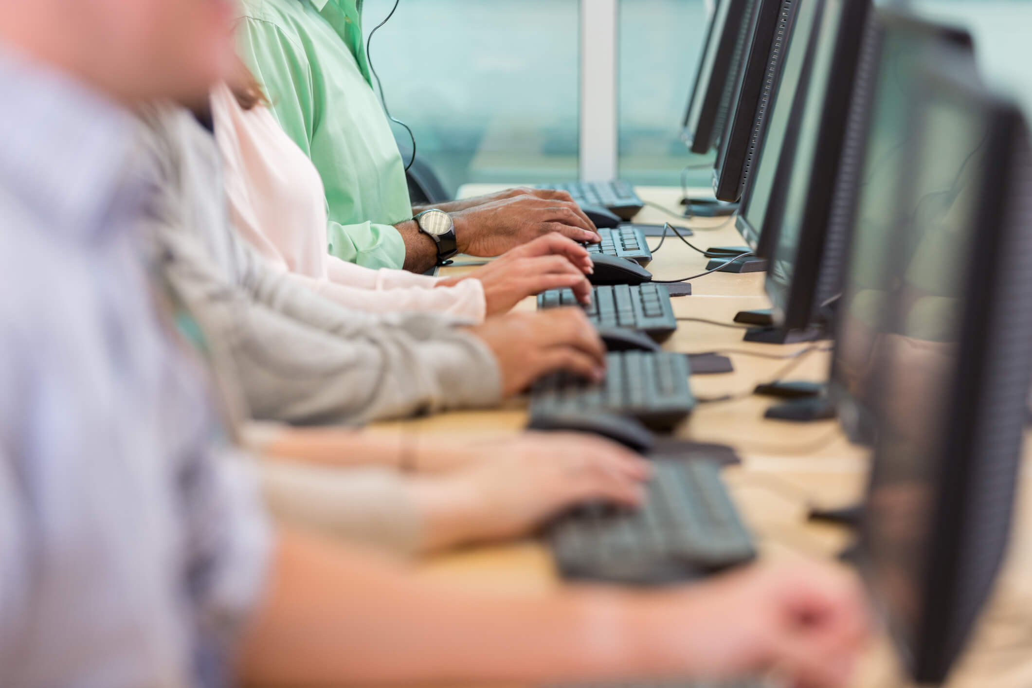 Several men working at an office, only hands typing on their computers visible