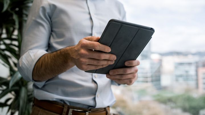 A man in a suit jacket holds a tablet computer in front of his torso