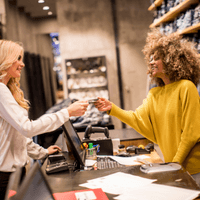 A customer hands a credit card to a retail employee at a point-of-sale counter