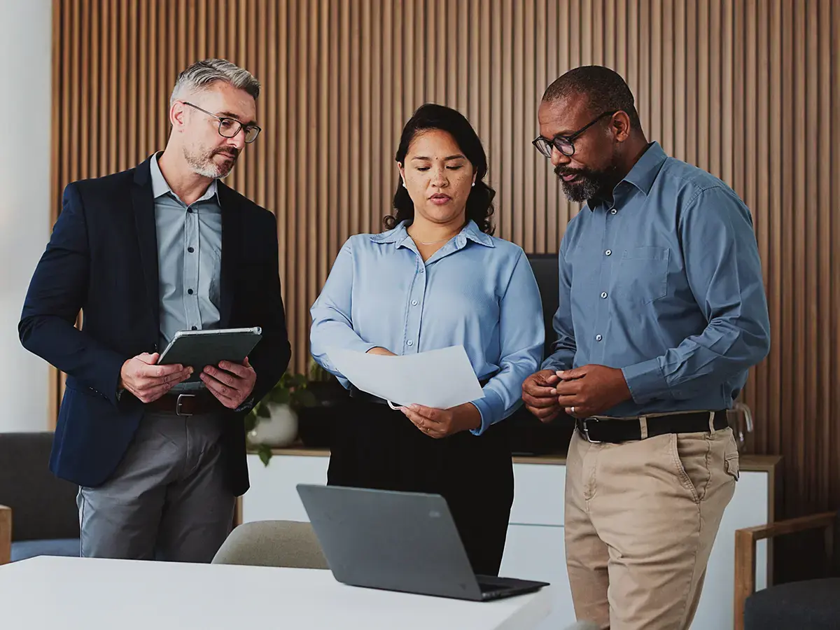Three business professionals review documents in a modern office