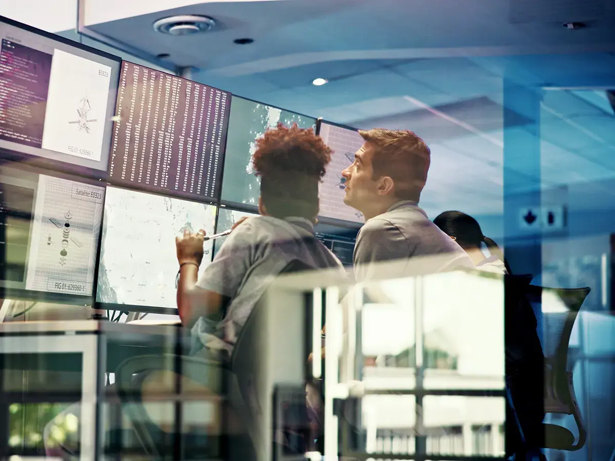 Two people are attentively looking at multiple computer monitors displaying data and graphs in a modern office